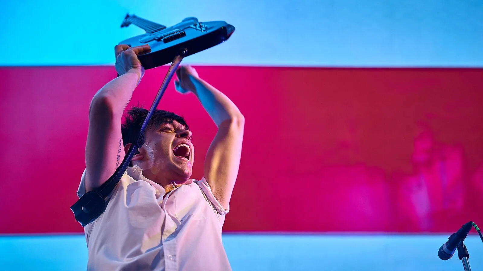 Musician performing with microphone headset in front of vibrant pink and blue backdrop during live concert performance