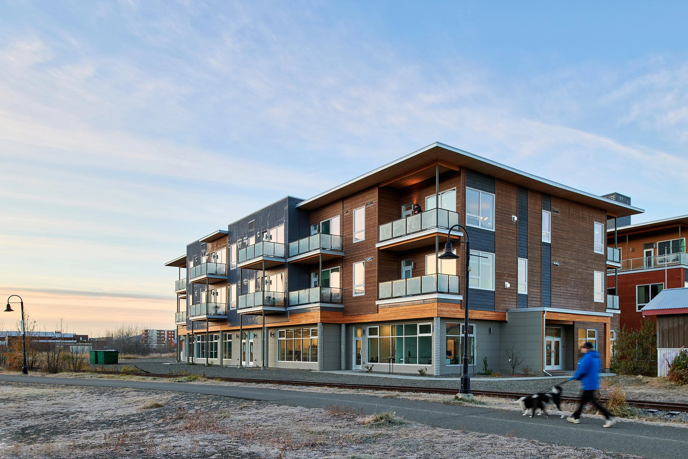 Modern apartment building in Whitehorse with a person jogging with a dog on the street in front